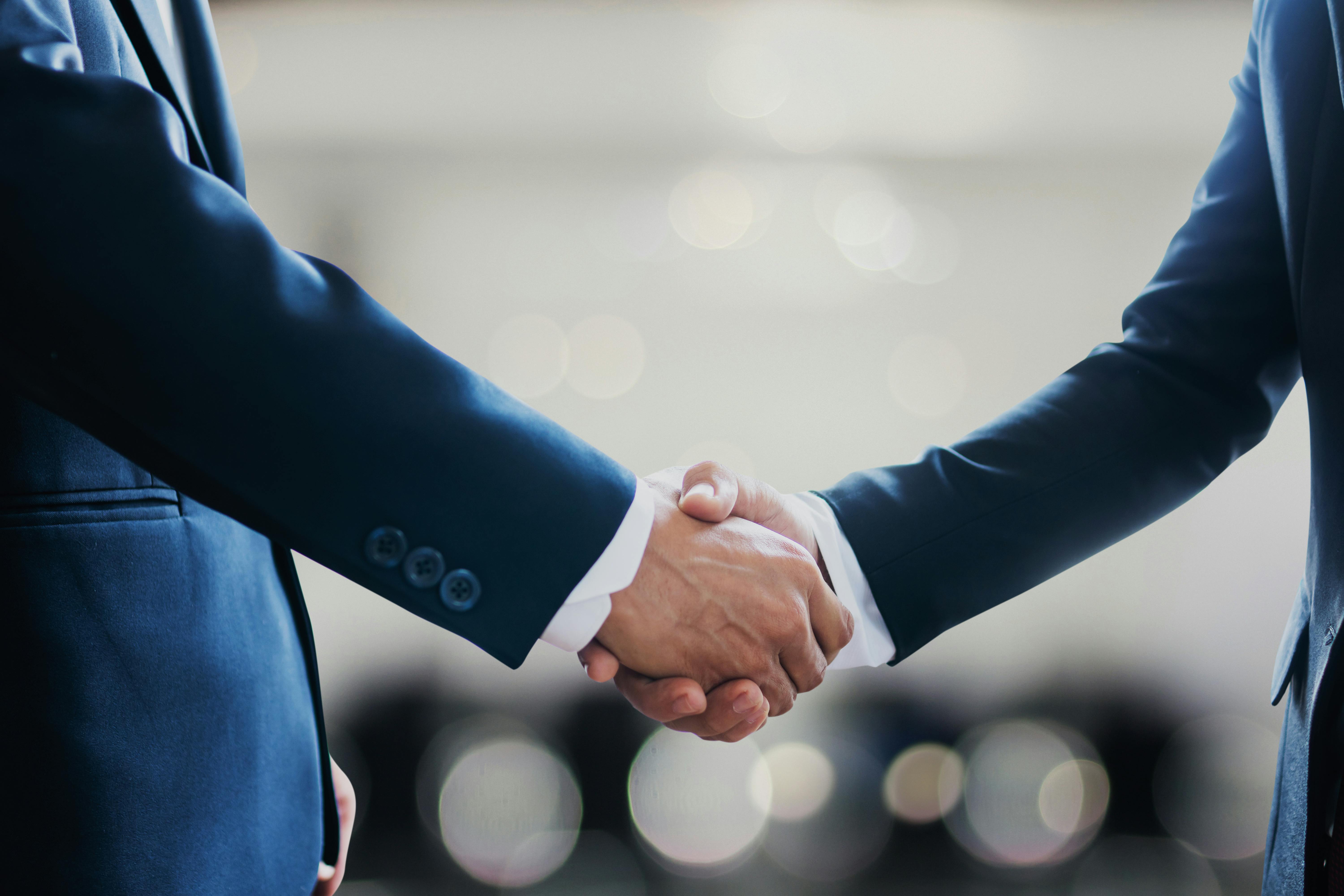 Two people in black business suits shaking hands, symbolizing partnership and agreement in a professional setting